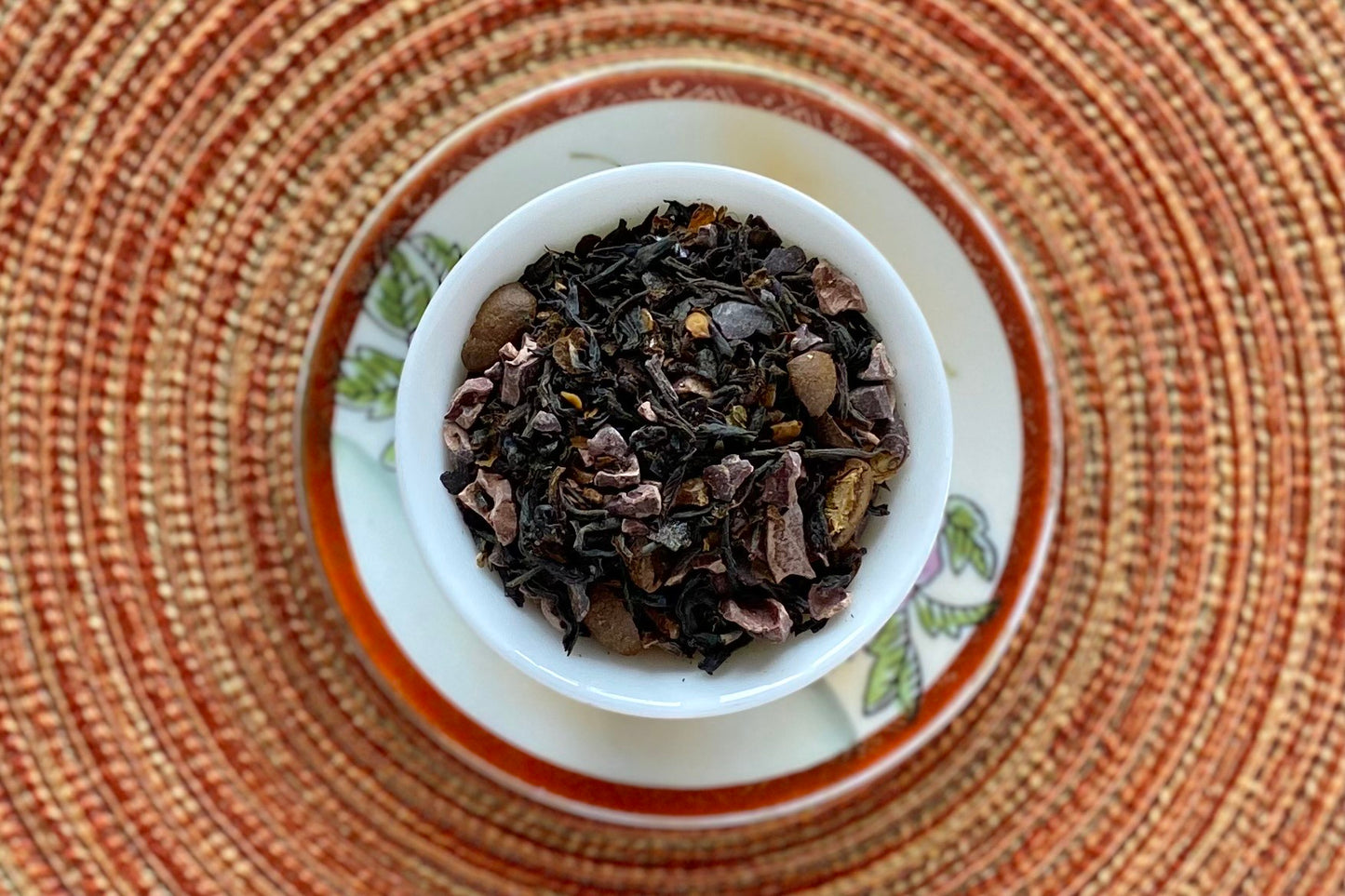 red and white teacup full of black tea, coffee beans, chili flake and cacao nib