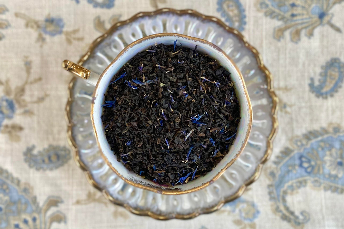 teacup full of black tea leaves with light touch of blue cornflower