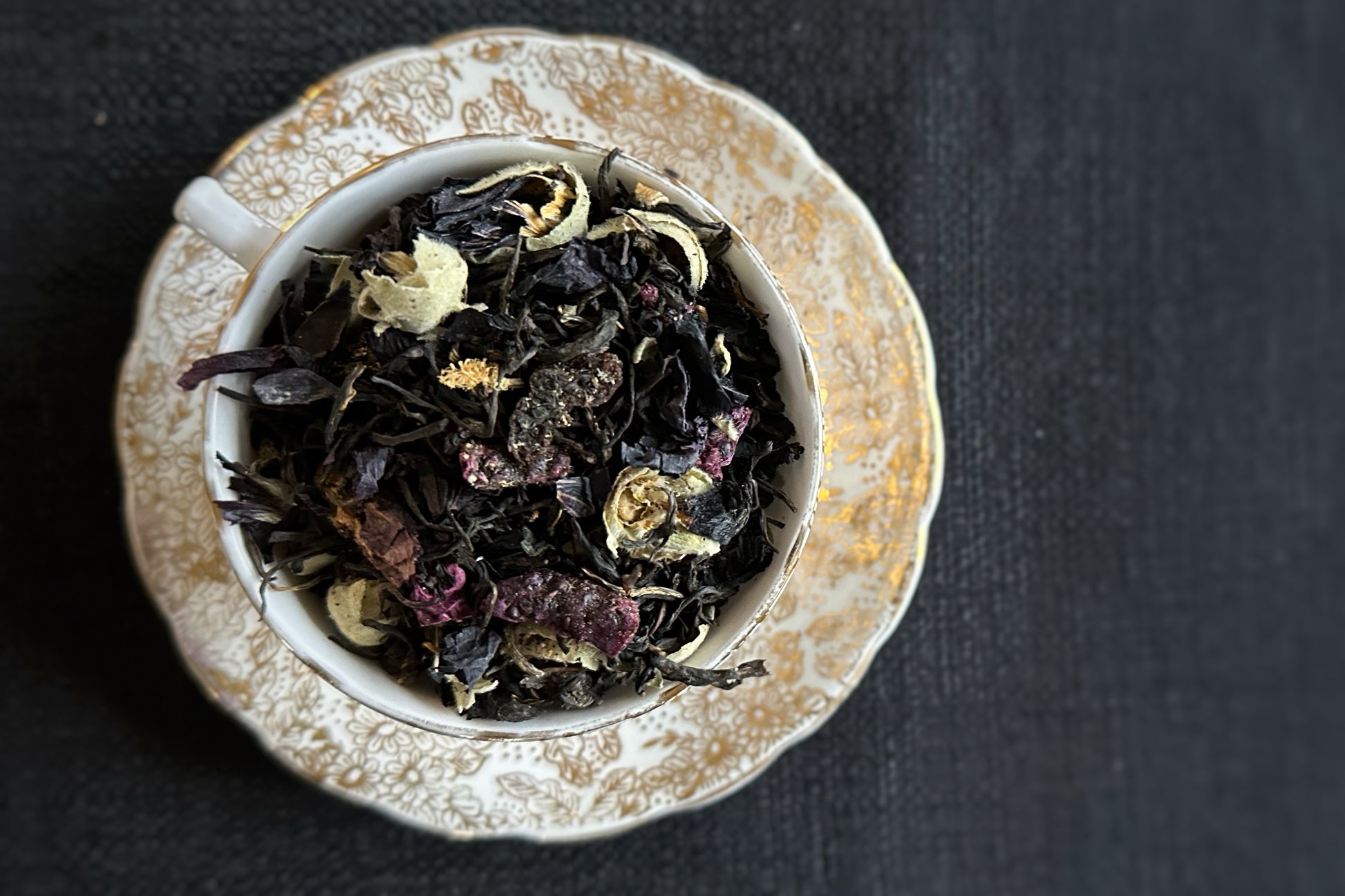 teacup full of tea leaves, fruits and flowers