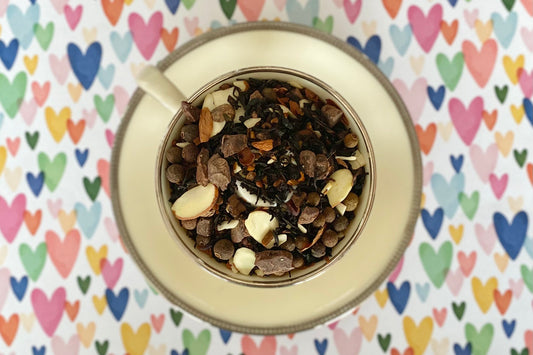 A teacup full of spices, chocolate, almonds and black tea on a colorful heart background