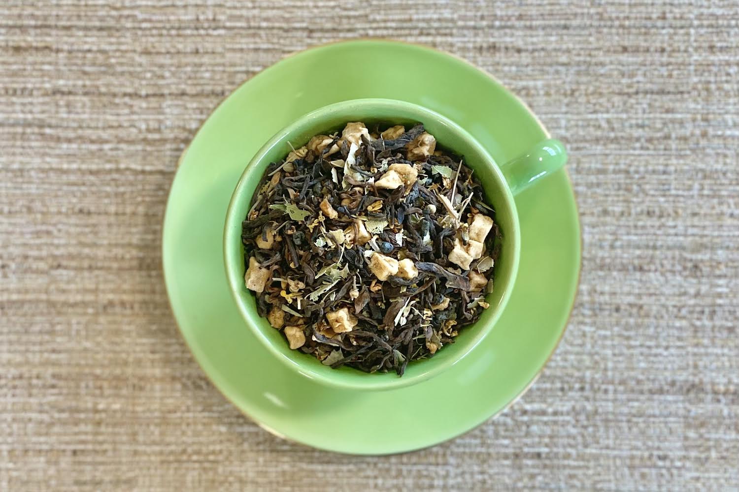 teacup full of dark leaf with apple, tiny yellow flowers, and green herbs