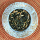 teacup full of rolled oolong leaf with orange blossoms and gold glitter